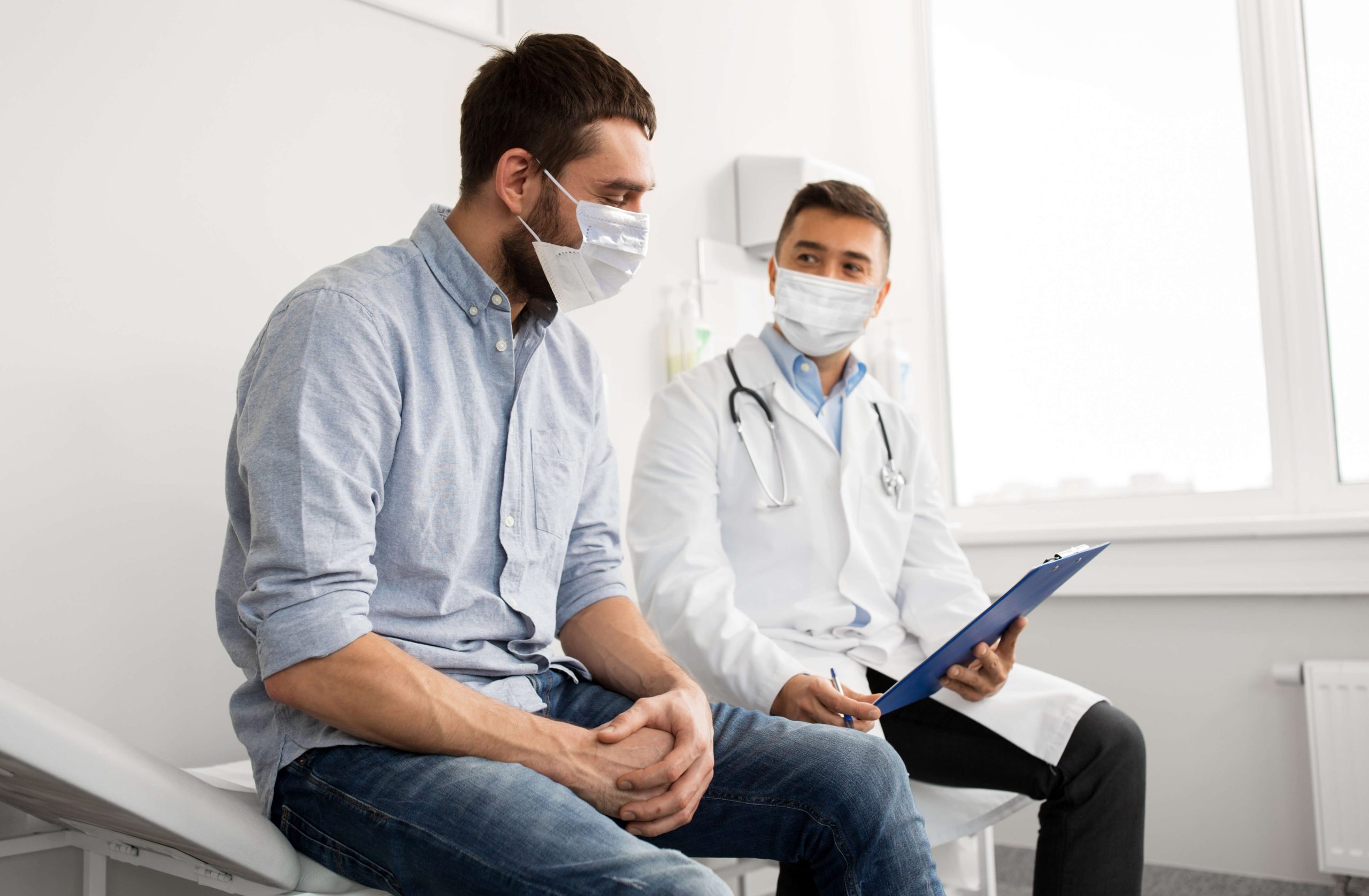 male doctor and male patient wearing masks and talking in exam room